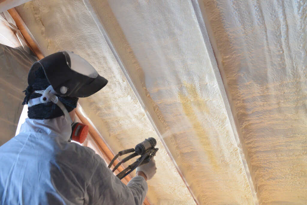 Person installing closed cell spray foam insulation in attic