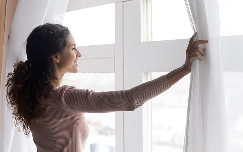 Happy woman opening curtains