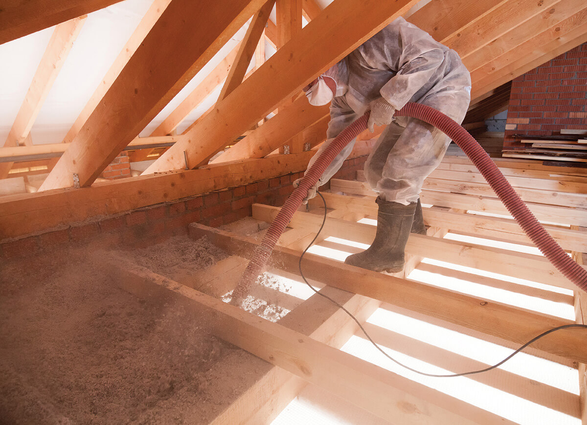 Worker installing blown-in insulation in attic