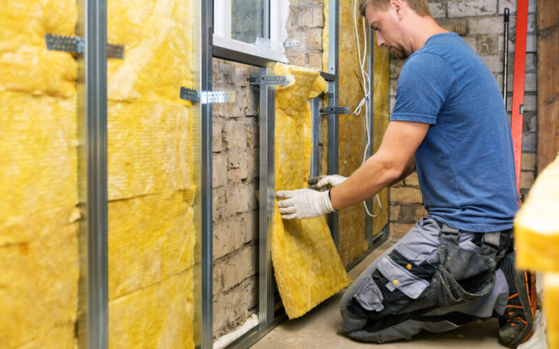 Man kneeling to install fiberglass insulation