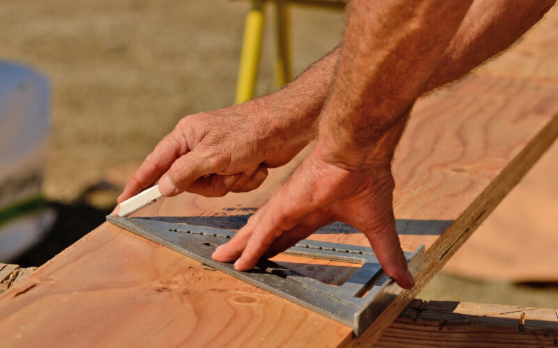 A contractor’s hands measuring cuts for a joist board