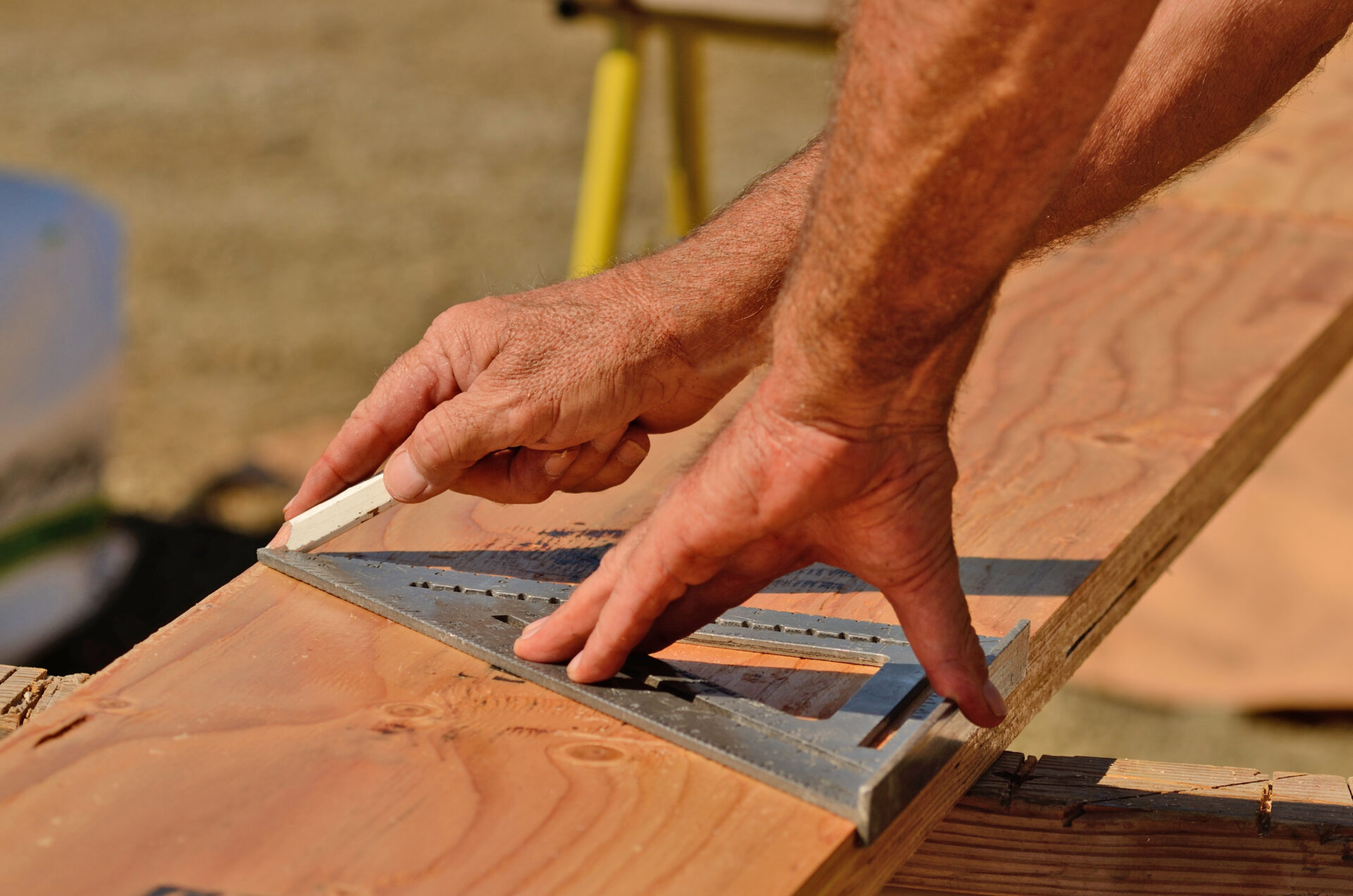 A contractor’s hands measuring cuts for a joist board