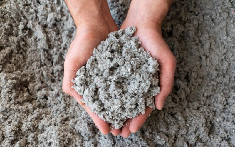 Two hands hold a pile of loose cellulose insulation