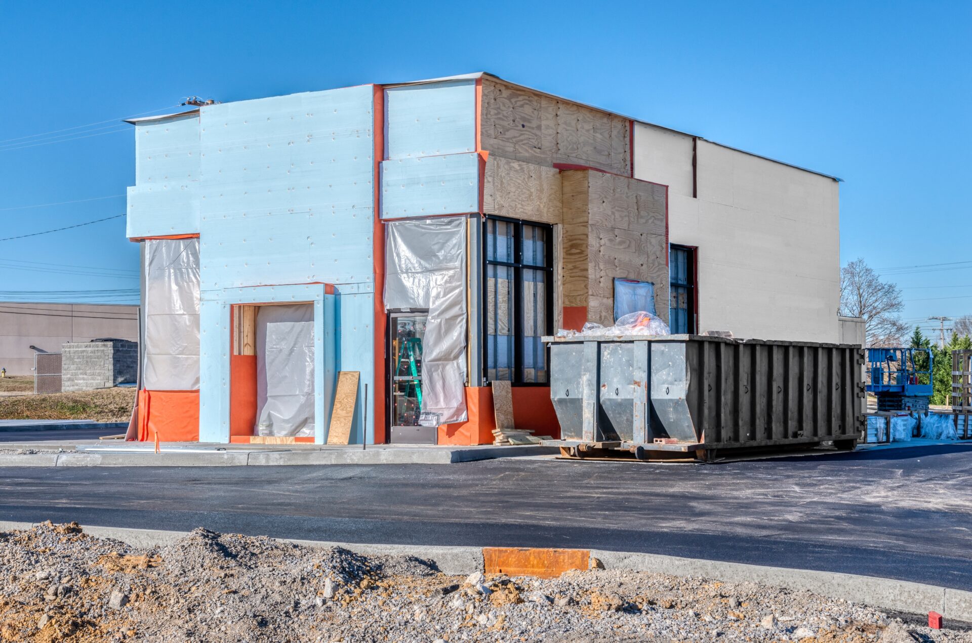 A small commercial building is under construction with plastic sheeting over the windows and dumpster in the parking lot
