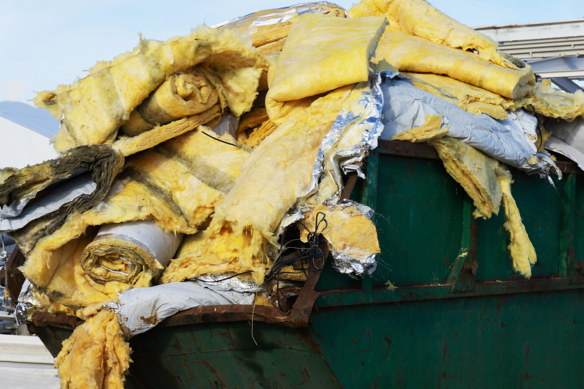 A green dumpster stacked high with discarded yellow insulation
